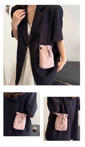 Detail of a light pink drawstring crossbody bag with black cord straps and spring buckle