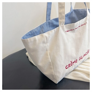 Detail shot of canvas tote bag featuring red embroidery and blue striped inner lining