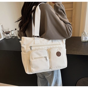Detail of white nylon tote bag with multiple zip pockets and wide woven shoulder strap