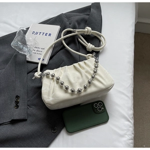 Detail der cremeweißen Plissee-Wolken-Tasche mit Silberperlenkette auf grauem Blazer