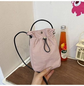 Detail of pink fabric drawstring bucket bag with black round handle and shoulder strap