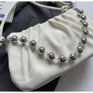 Detail der cremefarbenen Schultertasche mit Raffungen und polierten Silberperlen am Griff
