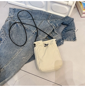 Detail of a beige canvas mini crossbody phone bag with drawstring and thin black strap