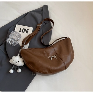 Detail of caramel lychee leather crescent bag with silver bow and plush cloud charm