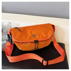 Detail view of vibrant orange crossbody saddle bag featuring metal logo and wide strap