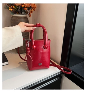 Détail d'un sac à main rouge en cuir ciré avec logo en métal et pendentif spirale