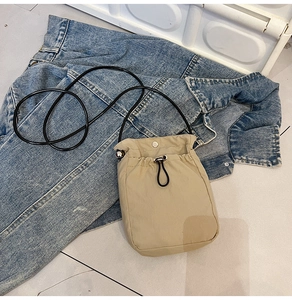 Detail of khaki fabric crossbody phone bag with drawstring and thin black strap on denim