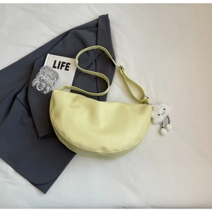 Flat lay of a light yellow half-moon crossbody bag with cloud charm on a grey blazer