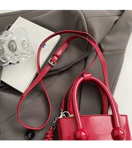 Détail du sac seau rouge au fini poli, décor de poignée sphérique et bandoulière fine