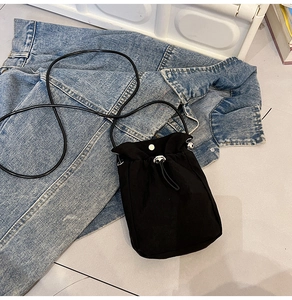 Close-up of black drawstring canvas bucket bag with silver hardware on denim jacket
