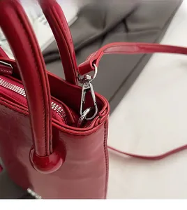 Détail macro du sac seau en cuir verni rouge avec zip argenté et mousqueton amovible