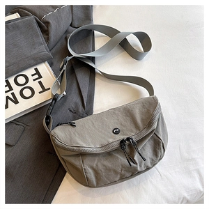 Close-up of a minimalist grey nylon half-moon bag with double zipper on white bedding