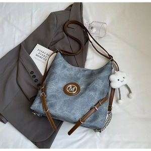 Detailed view of gray hobo bag with M logo, brown strap and plush cloud charm