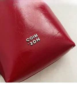 Gros plan détaillé du cuir verni rouge avec logo métallique argenté sur le sac à main