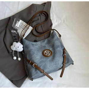 Close-up of vintage tote bag with metal M logo and white cloud plush charm on a bed