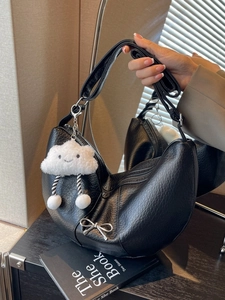 Retro black leather hobo bag with silver bow and plush cloud charm on a dark wooden table