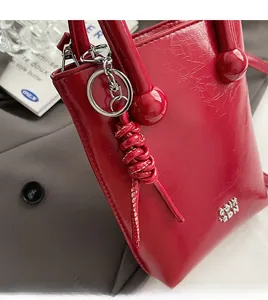 Détail du sac à main en cuir verni rouge avec logo argenté et nœud décoratif élégant