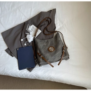 Detail of greyish-green large tote bag with brown leather trim and metal M logo on fabric