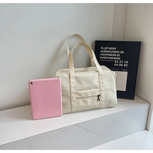 Détail du sac de voyage en toile beige avec poche zippée et larges poignées robustes