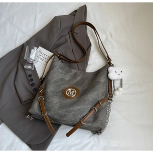 Detail of grey retro hobo bag featuring metal M logo and stylish silver chain ornament