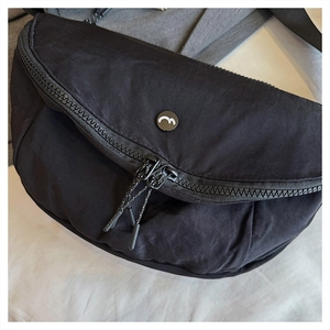 Close-up of lightweight black nylon crossbody bag featuring double zippers and round logo