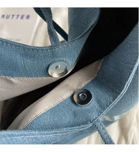 Detailed macro view of silver magnetic snap closure on a blue denim tote bag