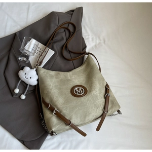 Detail of khaki canvas backpack featuring silver M logo and white cloud plush charm accessory