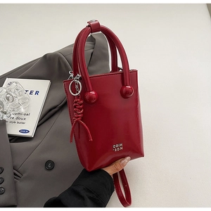 Détail du mini cabas en cuir verni rouge avec poignée boule et logo métallique chic