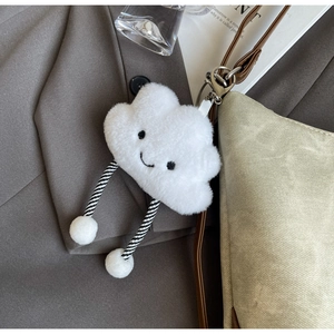 Close-up of a plush white cloud charm with a smiling face and striped legs on a bag