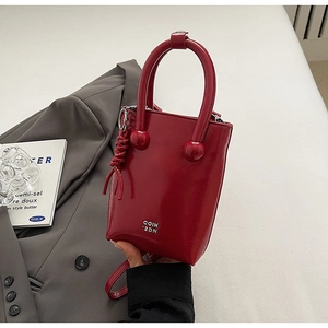 Détail du sac à main en cuir verni rouge avec finition brillante et poignée ronde unique