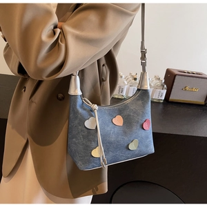 Detail of blue denim shoulder bag with colorful heart patches on a beige blazer