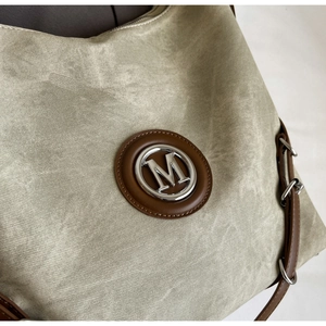 Detail of the green canvas tote bag showing the leather logo patch and metal M emblem