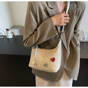 Close-up of beige shoulder bag with colorful heart patches on a beige suede texture