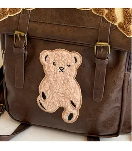 Close-up of vintage brown PU leather backpack with plush bear patch and metal buckles