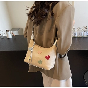 Detail view of beige suede shoulder bag featuring colorful heart-shaped embroidery patches