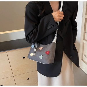 Detail of grey canvas crescent bag with colorful leather heart patches worn by a model