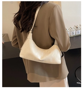Detail of a creamy white crescent underarm bag with glossy pleated texture on a shoulder view