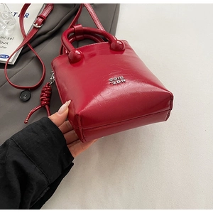 Détail du sac seau en cuir verni rouge avec logo en métal argenté et bandoulière fine