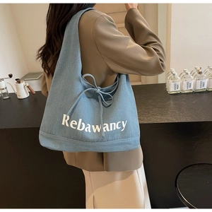 Detail of light blue denim tote bag with side drawstring bow and white text print