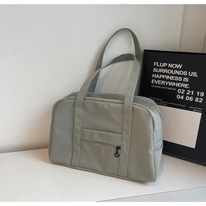 Gros plan d'un sac de voyage en nylon gris-vert pâle avec poche zippée dans un décor minimaliste