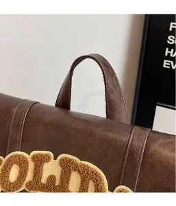 Detail view of brown leather backpack handle with neat stitching and chenille embroidery