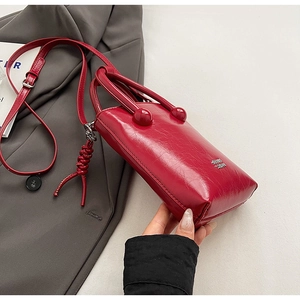 Vue détaillée du sac à main rouge en cuir brillant avec logo argenté et pendentif tressé