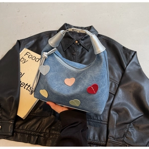Close-up of blue denim handbag featuring colorful heart patches and silver metal handles