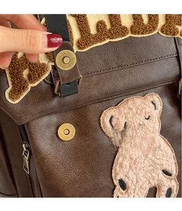Detail of vintage brown leather backpack featuring plush bear embroidery and brass magnetic buckle