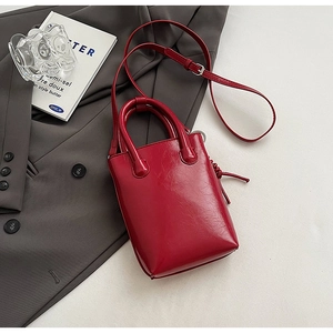 Vue détaillée du sac seau en cuir rouge brillant avec poignée et pompon sur veste