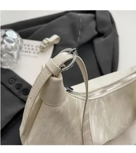 Close-up of adjustable long strap with silver ring buckle on textured cream leather bag