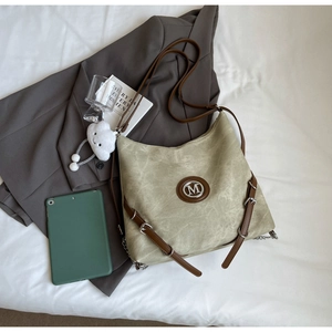 Detail of green hobo bag featuring brown leather straps and metal M logo on grey suit