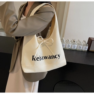 Close-up of cream canvas tote bag featuring black letter print and decorative bow detail
