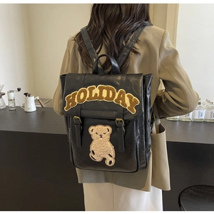 Detail of black PU leather backpack featuring plush holiday lettering and bear patch