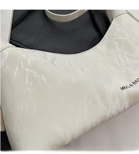 Close-up of cream white underarm bag showing natural marble texture and MKXQ brand logo